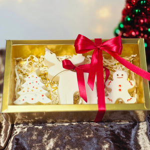 Kerst cadeauset met witte figuurkaarsen: rendier, kerstboom en gingerbread in gouden doos met rood lint en gouden belletjes